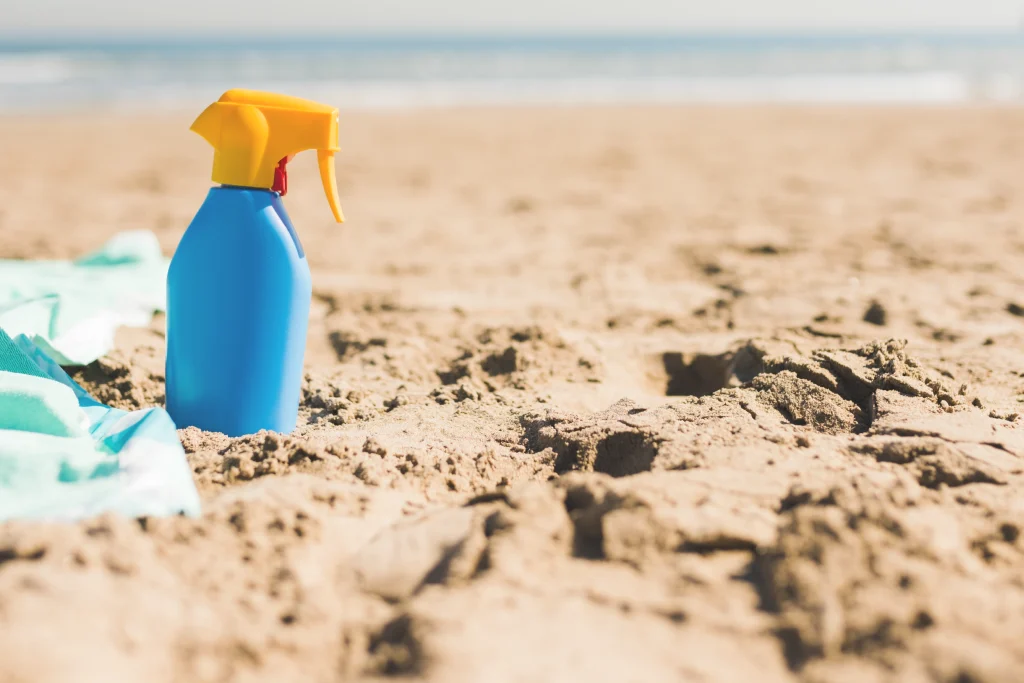 Frasco de protetor solar sobre uma toalha na praia, imagem do artigo da Blue Lavandarias sobre como tirar manchas de protetor solar da roupa.